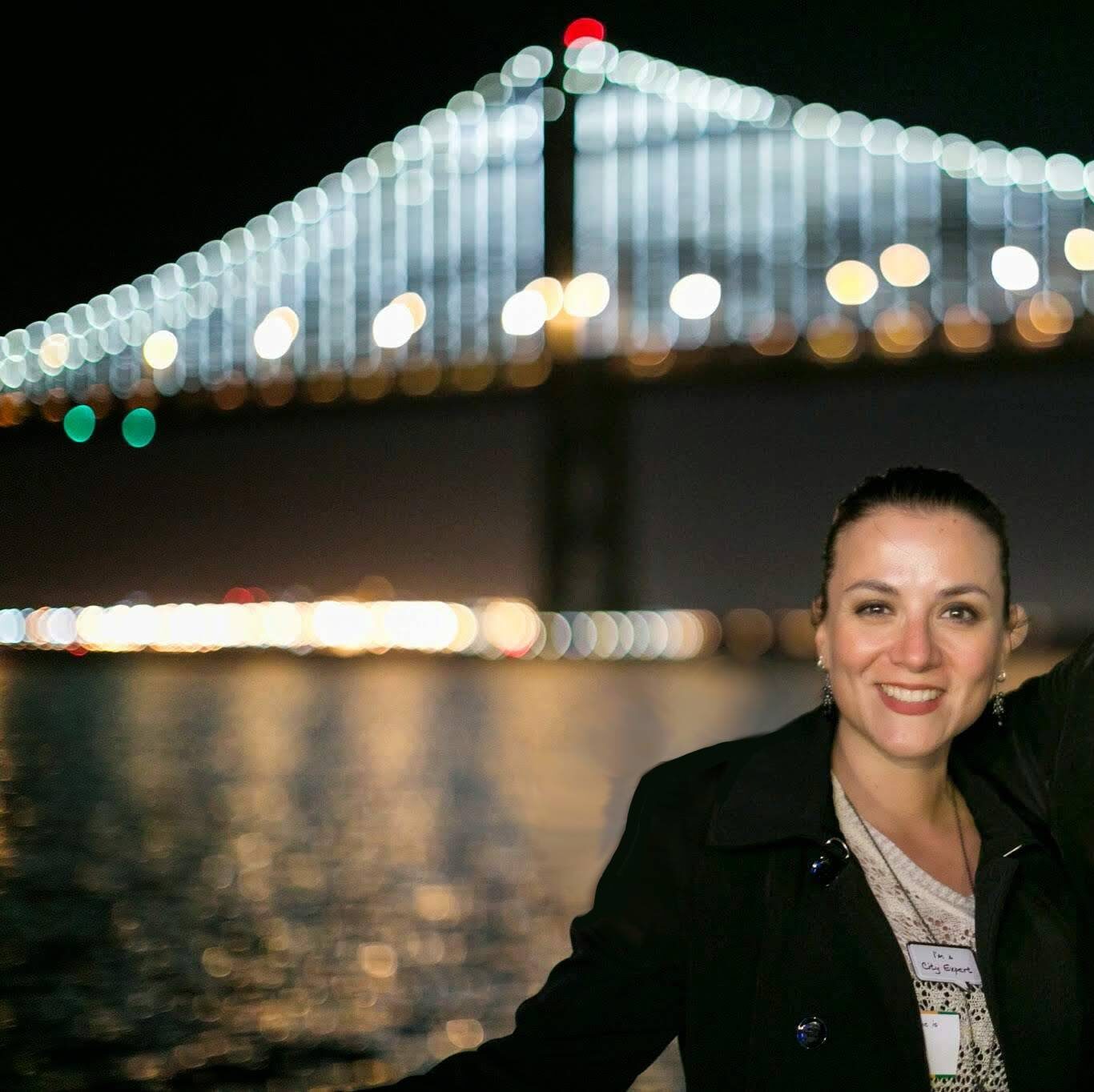 Me out and about on a night cruise in the San Francisco bay area. I'm wearing a black jacket, my hair is in a bun, and you can see an unfocused bridge behind me