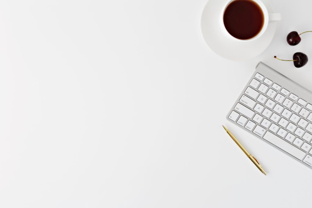 Text over a picture of a white desk with a cup of coffee, a keyboard, a gold pen