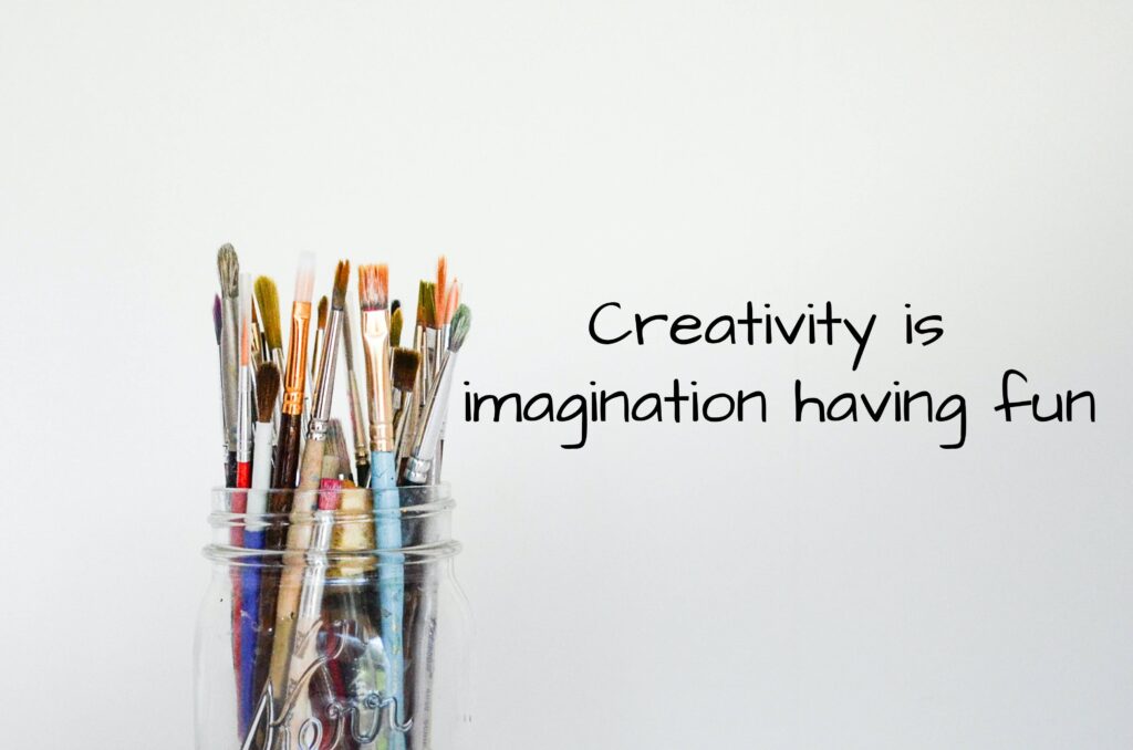 "Creativity is imagination having fun" written next to a mason jar with paint brushes. Photo by Debby Hudson on Unsplash